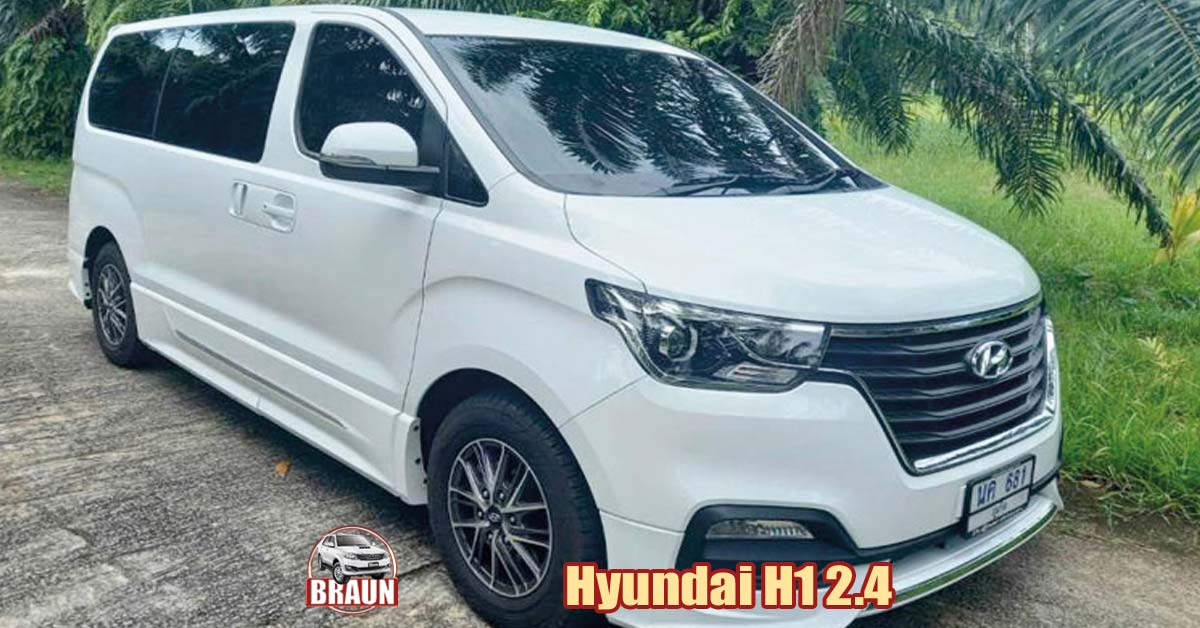white hyundai h1 2.4 litre 12 seater minibus rental in phuket parked on a concrete road beneath palm fronds with jungle in the background