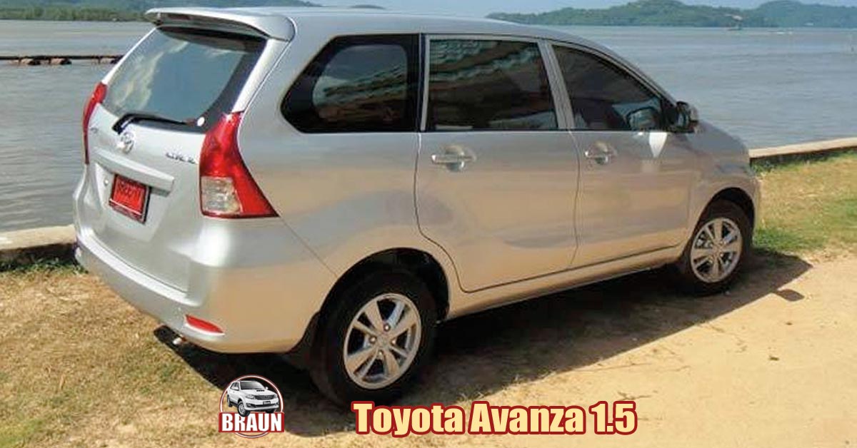 silver toyota avanza 1.5 litre people carrier parked next to a sea wall in the phuket sunshine on sand and sea grass with a wooden pier, sea and forested coastline in the background