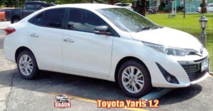 white toyota yaris 1.2 rental car phuket parked ready for collection at the front of hotel with a toyota hilux in black at the rear, behind is a lawned area with seating and lighting